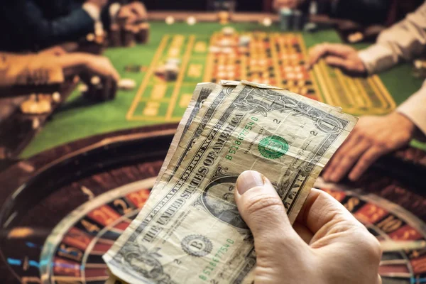 hand holds dollars on the background of the casino and roulette, gambling, entertainment