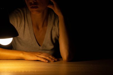 Karanlık bir odada masa lambasının ışığında oturan bir kız.