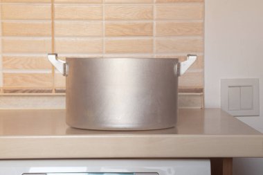 İki saplı büyük bir alüminyum tencere bir evin duvarına karşı bir mutfak masasında duruyor.