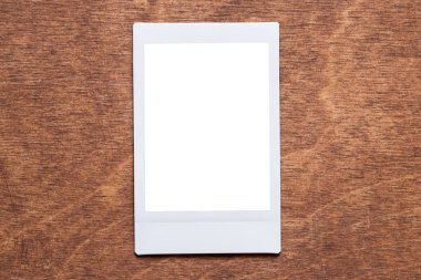 Anlık fotoğrafçılık tarzında boş beyaz fotoğraf şablonu, tasarım ve resim eklemek için kullanılan ahşap bir tablo üzerinde yatar