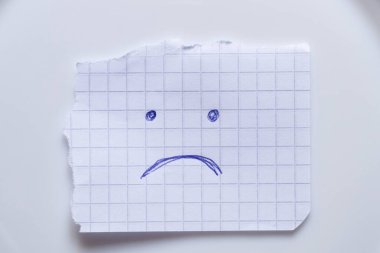 Mavi kalemle çizilmiş kareli bir sayfa beyaz arka planda üzüntünün, ruh halinin ve ifadesinin sembolü olarak yatar.