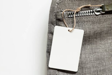 İpte beyaz boş etiket, beyaz arka planda gri sırt çantasında tasarım için yakın plan modeli olarak yatar