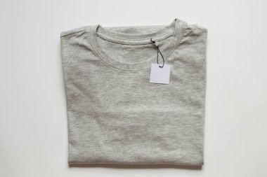 İpin üzerindeki beyaz boş etiket, beyaz arkaplandaki gri tişörtün üzerinde tasarım için yakın plan modeli olarak duruyor.