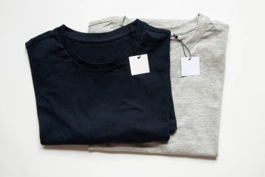 Tasarım için yakın plan olarak beyaz arkaplanda etiketleri olan iki gri ve mavi tişört.