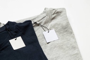 Tasarım için yakın plan olarak beyaz arkaplanda etiketleri olan iki gri ve mavi tişört.