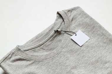 İpin üzerindeki beyaz boş etiket, beyaz arkaplandaki gri tişörtün üzerinde tasarım için yakın plan modeli olarak duruyor.