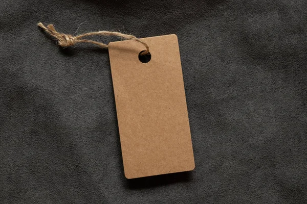 İpin üzerindeki kahverengi boş bir etiket, yakın plan tasarım için gri tüylü bir kumaşın üzerinde duruyor.