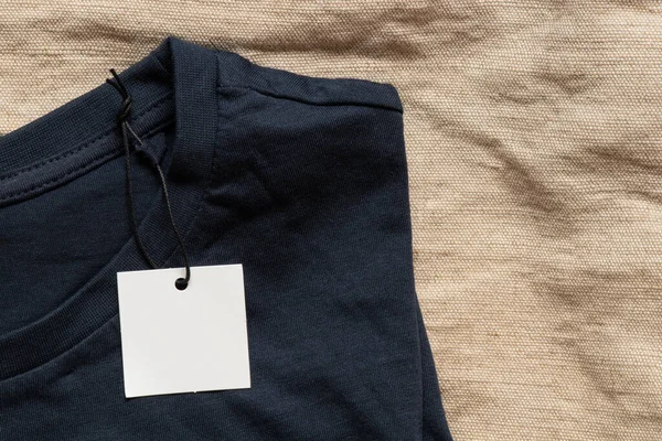 İpte beyaz boş etiket tasarım için yakın plan olarak bej kumaşta mavi tişörtte yatıyor.