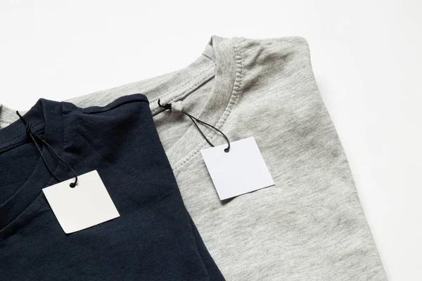 Tasarım için yakın plan olarak beyaz arkaplanda etiketleri olan iki gri ve mavi tişört.