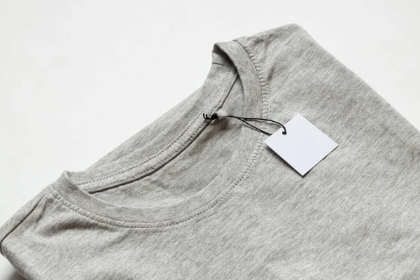 İpin üzerindeki beyaz boş etiket, beyaz arkaplandaki gri tişörtün üzerinde tasarım için yakın plan modeli olarak duruyor.
