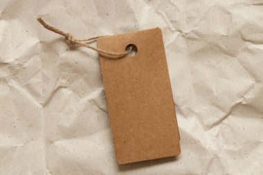 İpin üzerindeki kahverengi boş bir etiket, kahverengi buruşmuş kağıdın üzerinde tasarım için bir model olarak duruyor.