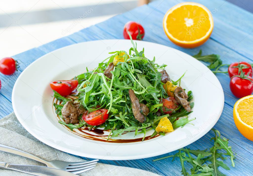 Salad with chicken liver, arugula, orange and tomatoes on a plate