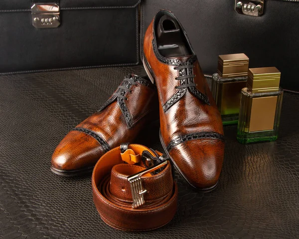 Composição de um par de sapatos castanhos masculinos, duas garrafas de perfume masculino e cinto de calças masculinas no fundo das maletas pretas masculinas — Fotografia de Stock