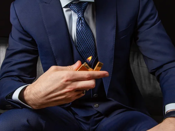 Klasik takım elbiseli bir adam siyah deri bir kanepeye oturur ve pahalı bir çakmak gösterir