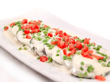 Dilimlenmiş ve kızarmış patlıcan üzerine beyaz sos serpilmiş ve doğranmış yeşil soğan ve dikdörtgen bir tabakta taze domatesler serpiştirilmiş. Yaklaş, seçici odaklanma