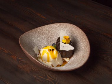 Bir kepçe dondurma, nane yaprağı ve yabani böğürtlen ve çiçeklerle süslenmiş sıcak çikolatalı brownie. Terk edilmiş tahtaların ahşap arka planında. Yaklaş, seçici odaklanma