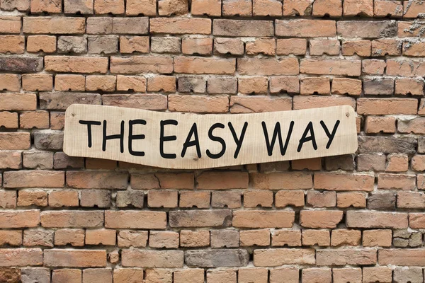 The Easy Way written on wooden sign on brick wall background.