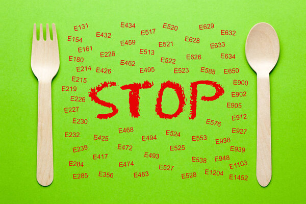 Stop and the code E-additives written on green paper sheet with spoon and fork. Banned Additives Diagram.