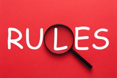 Kırmızı bir arka plan ve Büyüteç Camı yazılı kurallar. İş kavramı