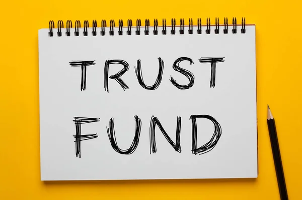 TRUST FUND written on notepad with pencil on yellow background. Business concept.