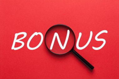 Kırmızı arka plan ve büyüteç üzerine yazılmış ikramiye. İş konsepti.