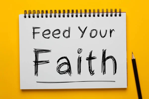 Feed Your Faith written on notepad with pencil on yellow background. Business concept.