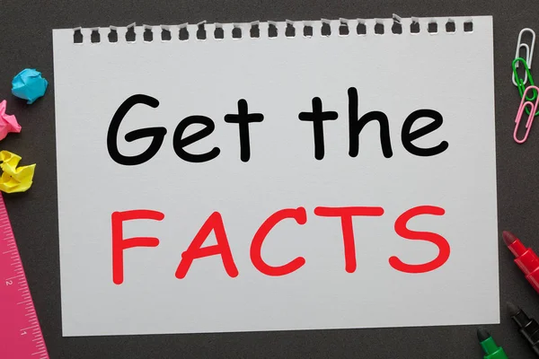 Get the Facts written on notebook paper and office supplies on black background. Business concept.