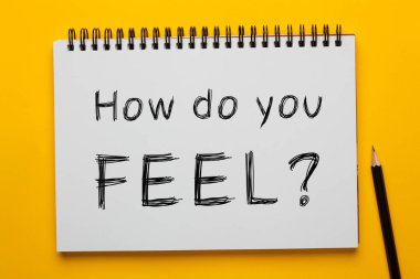 Nasıl hissediyorsun soru üzerinde Yazılı not defteri ile sarı zemin üzerine kalem. İş kavramı.