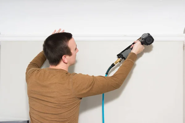 Caucasian man installs trims with nail gun — Stock Photo, Image