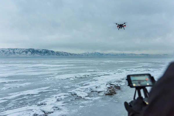 Adam donmuş göl üzerinde siyah drone helikopter uçar