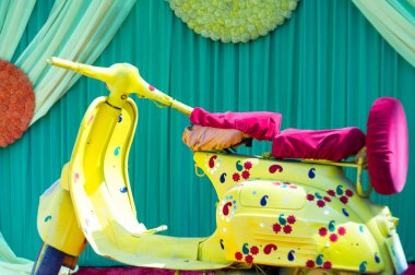 Sarı motor scooter motosiklet evlilik, olay, kutlama için yaprakları dekorasyon öğesi ile boyalı. Kırmızı kadife koltuk Hint kasaba nostalji verir ile yeşil mavi perde önünde park etmiş