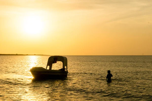一个人在远处为一条有落日的船抛锚的剪影 — 图库照片