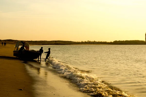 Silueta mužů tlačí turistickou rybářský člun do oceánu na pláži Gujarat — Stock fotografie