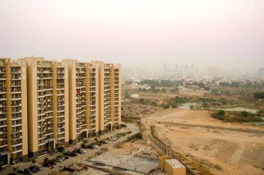 Skyscrapers in gurgaon looking out over barren land and a village clipart