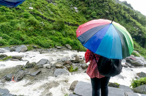 Chica con paraguas colorido mirando hacia fuera sobre un río que fluye con las colinas cubiertas de plantas detrás de ella —  Fotos de Stock