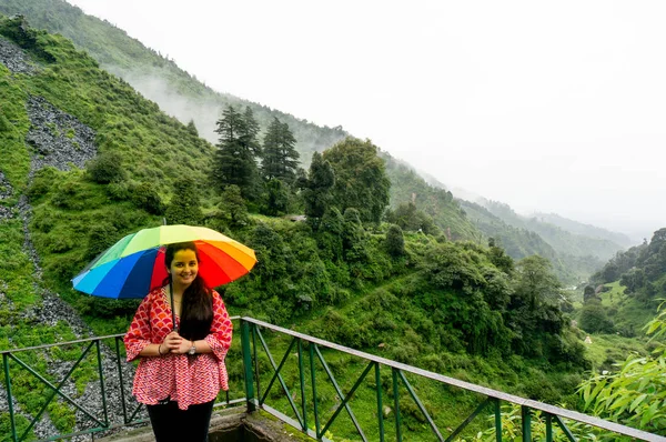 Młody indyjski dziewczyna stoi aparat fotograficzny z kolorowym parasolem w zakładzie pokryte pochmurno mgliste wzgórza — Zdjęcie stockowe