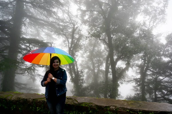 Joven chica india con un colorido paraguas de pie frente a espeluznantes árboles de niebla —  Fotos de Stock