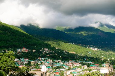 Hindistan 'daki tepe istasyonu binalar ve çimlerle kaplı tepeler üzerine bulutlar düşüyor.