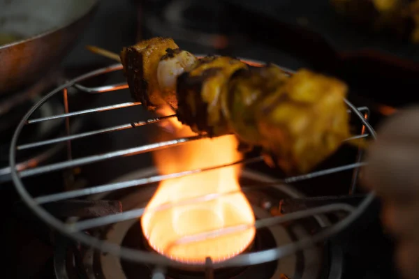 Chupito de paneer requesón quemado tandoori carbonizado a la parrilla sobre una parrilla de comida y una estufa de gas con llamas y quemando el queso, pimientos, cebollas y tomates — Foto de Stock