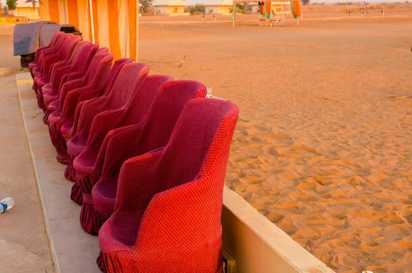 Primer plano de sillones de bastón de muddha rojo sofás con pequeñas paredes de ladrillo amarillo para los visitantes de asientos durante una actuación con arena del desierto en el fondo — Foto de Stock
