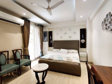 Geniş açılı modern büyük yatak odası, zarif yatak odası, küçük kahve masası, sandalyeler ve vantilatör.