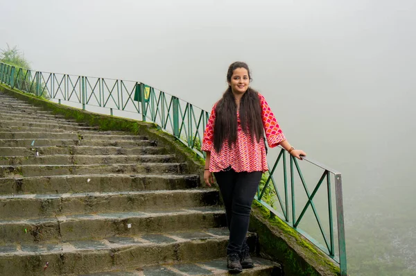 Chica india joven en un vestido rojo de pie en una serie de escaleras que conducen a las caídas de bhagsu en McLeodganj en la India himachal —  Fotos de Stock