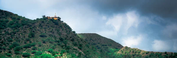 Храм гінду на пагорбі, вкритому рослинністю з вежею і шпилем, добре видно на відстані з тлом темних мусонних хмар, знятих в Раджастані Індії. — стокове фото
