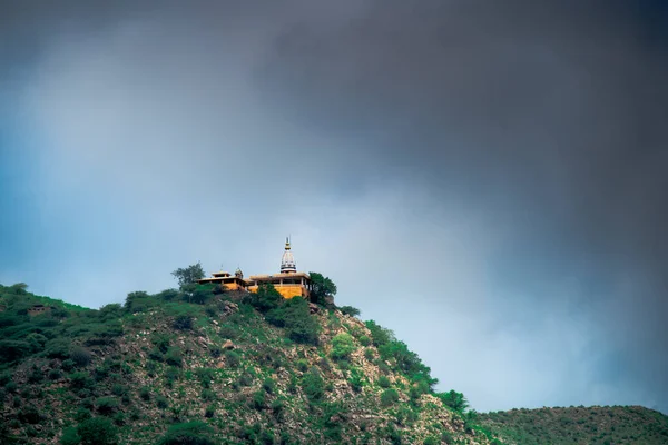 Храм гінду на пагорбі, вкритому рослинністю з вежею і шпилем, добре видно на відстані з тлом темних мусонних хмар, знятих в Раджастані Індії. — стокове фото