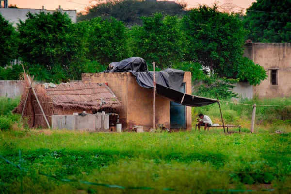 Atardecer tiro de granjero sentado en una cuna fuera de su casa de paja permanente y improvisada comer mientras los árboles en el fondo —  Fotos de Stock