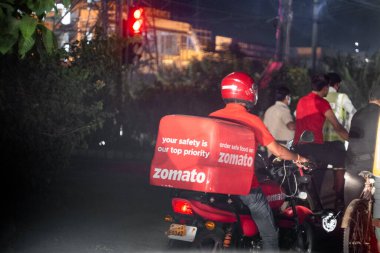 Zomato yemek dağıtım elemanı kırmızı kasklı, gömlekli ve yemek kutusuyla yiyecek teslimatı için yolda giderken Hint firması daha fazla şehre yayılıyor.