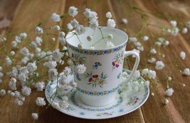 Antika porselen closeup gypsophila paniculata kahverengi ahşap masa küçük beyaz çiçekleri ile süslenmiş boyalı çok renkli çiçek süsleme ile tabağa Kupası. seçici odak.