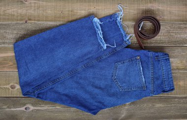 Yüksek bel kadınların üstten görünüm mavi katlanmış kot pantolon ve kahverengi ahşap zemin üzerinde bir deri kemer. Gençler kavramı. Genç. 