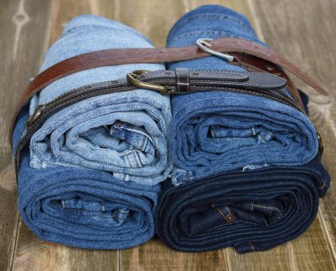 katlanmış mavi kot pantolon doğal deri kayış üzerinde ahşap arka plan ile bir yığın closeup. kot moda. Gençler simgesi.