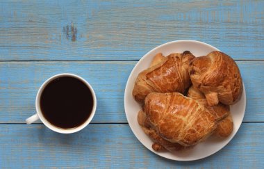 kahve ruh. Kahve zamanı. bir fincan kahve ve bir plaka ile altın kabuk ile taze pişmiş kruvasanlar, mavi, retro ve ahşap bir masa bir bardakta bir kruvasan yanındadır